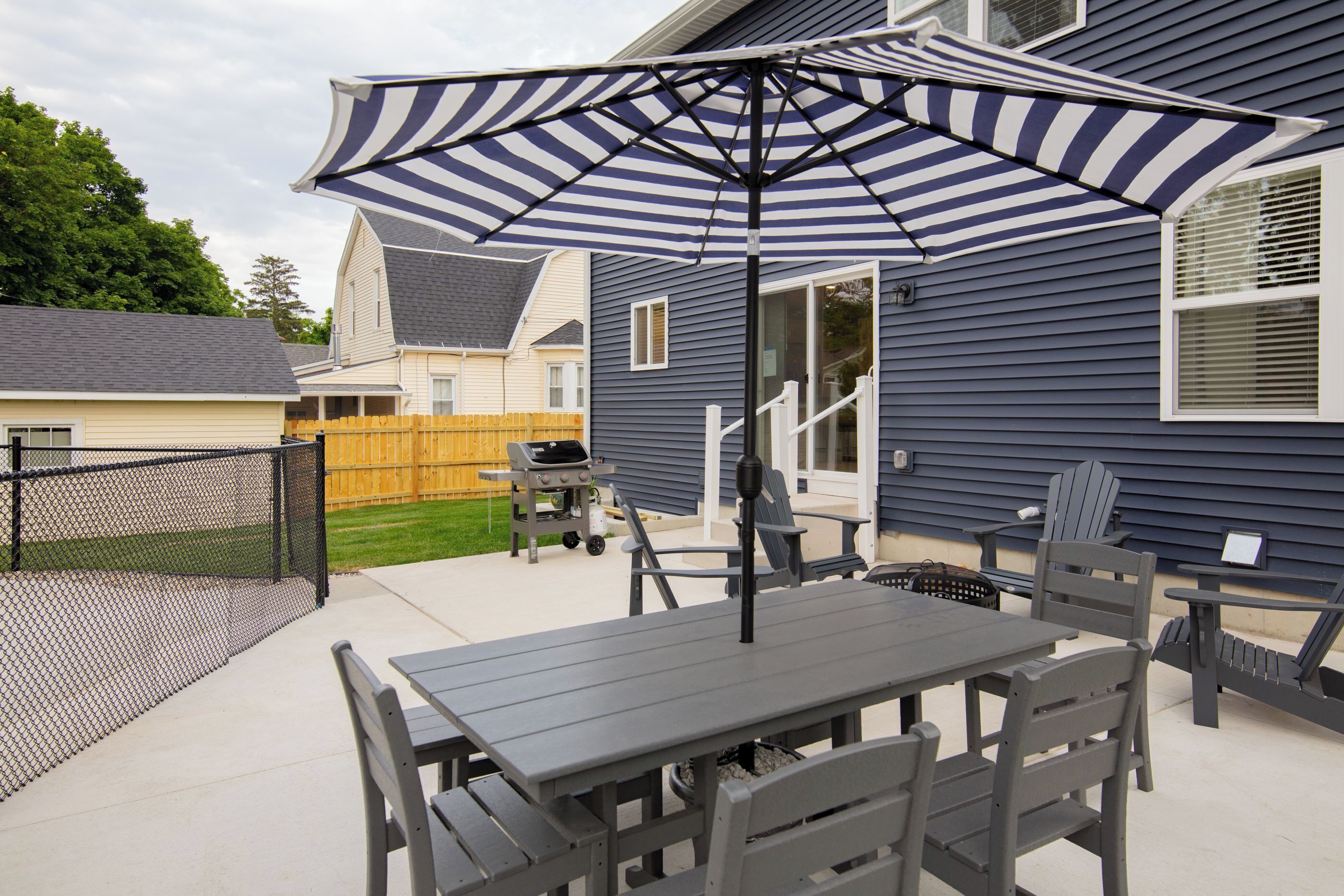 An outdoor patio with a table and chairs, a striped umbrella, and a grill.
