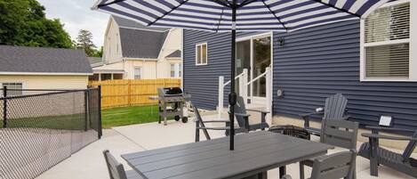 An outdoor patio with a table and chairs, a striped umbrella, and a grill.