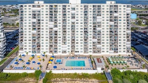 A high-rise hotel with multiple balconies, a swimming pool, and a parking area.
