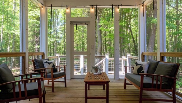 Un espace extérieur aménagé, abrité et doté de mobilier en bois, avec de grandes fenêtres donnant sur une forêt.