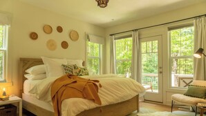 Une chambre spacieuse avec un grand lit, de nombreuses fenêtres et une vue sur la verdure environnante.