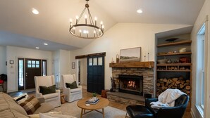 Un salon chaleureux avec une cheminée, un lustre et des fauteuils confortables.