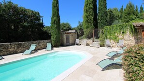 Ein Pool mit Liegestühlen, umgeben von hohen Bäumen und einer Steinmauer.