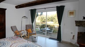 Ein Zimmer mit einem Bett, zwei Sessel, einer Stehlampe und Blick auf eine Terrasse mit Tisch und Stühlen.