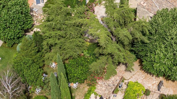 Eine Vogelperspektive zeigt einen Innenhof mit Swimmingpool, umgeben von Steingebäuden mit Ziegeldächern und üppiger Bepflanzung.
