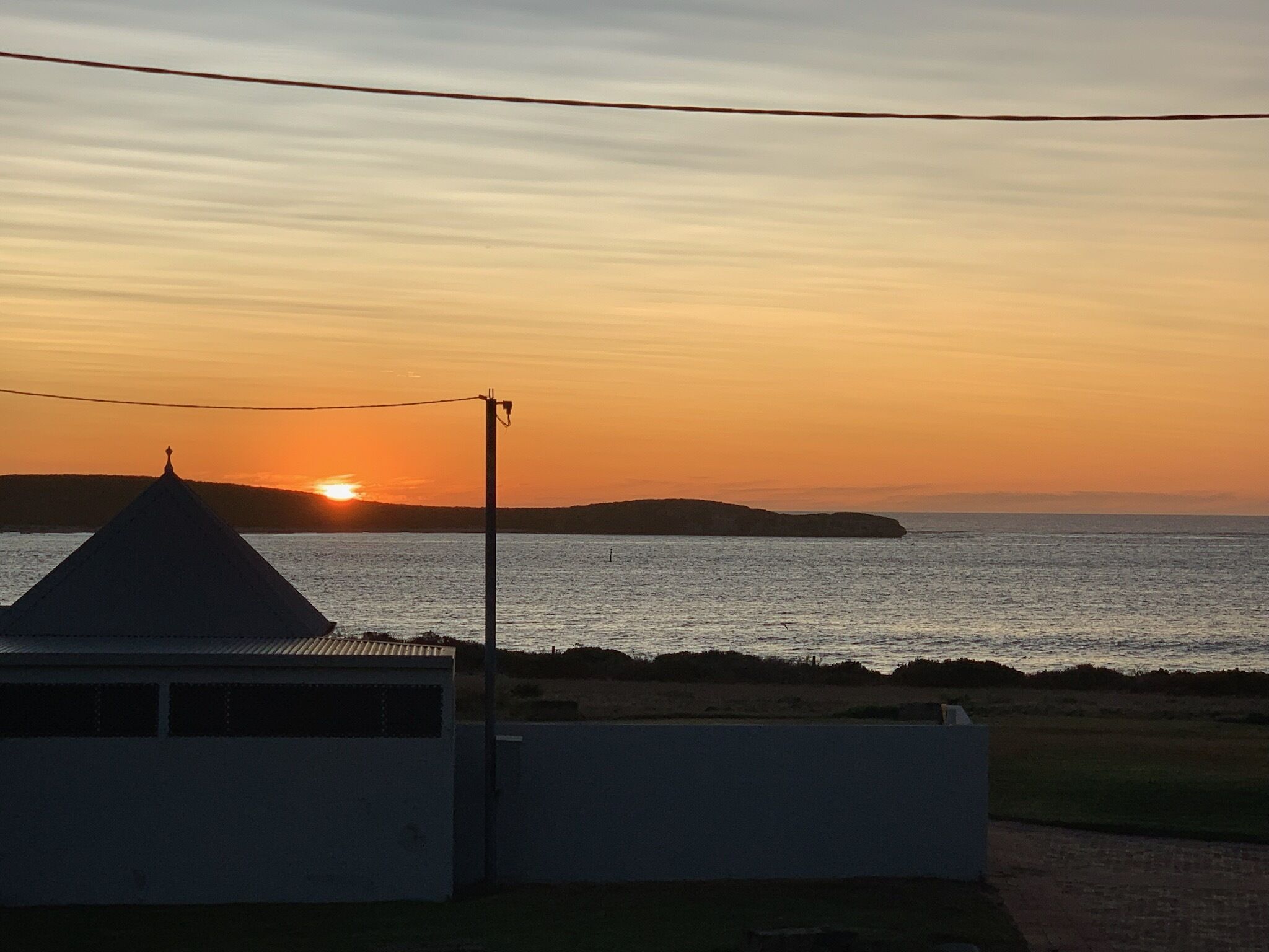 A coastal sunset view with a building silhouette and a clear sky.