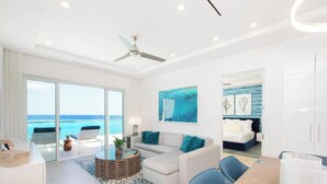A modern hotel room with a large balcony, a sofa, a dining table, and a bed. - Rum Point Resort 408 by Grand Cayman Villas (Grand Cayman)