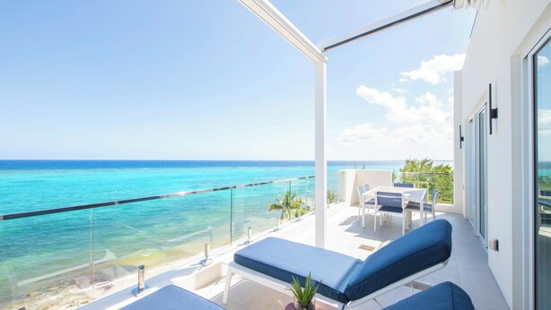 A balcony with a view of the ocean, lounge chairs, and a small table with a plant. - Rum Point Resort 408 by Grand Cayman Villas (Grand Cayman)