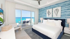 A modern hotel room with a large bed, a balcony with a view of the ocean, and artwork on the wall. - Rum Point Resort 408 by Grand Cayman Villas (Grand Cayman)