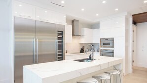 A modern kitchen with a large island, stainless steel appliances, and bar stools. - Rum Point Resort 304 by Grand Cayman Villas (Seven Mile Beach)