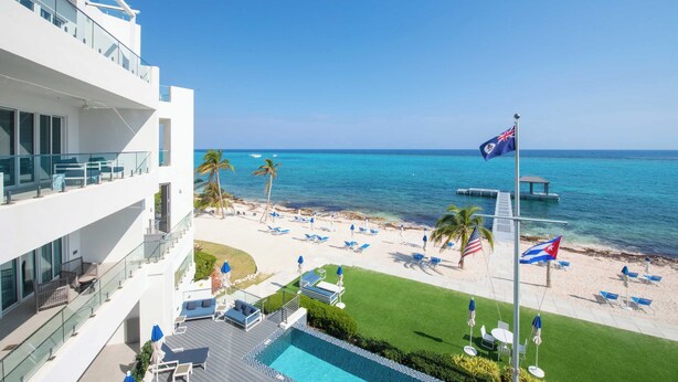 A hotel with a pool, lounge chairs, and a view of the beach and ocean. - Rum Point Resort 304 by Grand Cayman Villas (Seven Mile Beach)