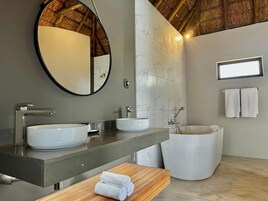 Uma casa de banho moderna com um espelho redondo, duas pias, uma banheira e um lavatório de madeira.
