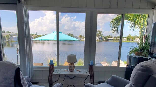 A room with a view of a lake, two chairs, a table with a lamp, and a ceiling fan. - Lakeside Cottage. Serene, Tranquil home. 2.mi.(4)mins from the Beach. Sleeps 3.  (Naples)