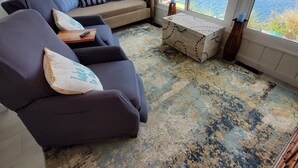 A cozy living room with a sofa and armchairs, a wooden chest, and a view of a lake. - Lakeside Cottage. Serene, Tranquil home. 2.mi.(4)mins from the Beach. Sleeps 3.  (Naples)