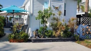 A white single-story building with a small porch, surrounded by tropical plants and a palm tree. - Lakeside Cottage. Serene, Tranquil home. 2.mi.(4)mins from the Beach. Sleeps 3.  (Naples)