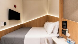 Hotellihuone, jossa on sänky, työpöytä, tuoli, televisio, yöpöytä ja ohjauspaneeli.