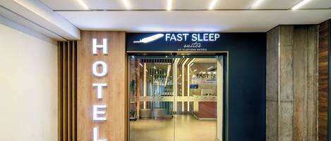 Entrada de hotel com uma placa indicando 'FAST SLEEP SUITES BY SLAVIERO HOTELS'.