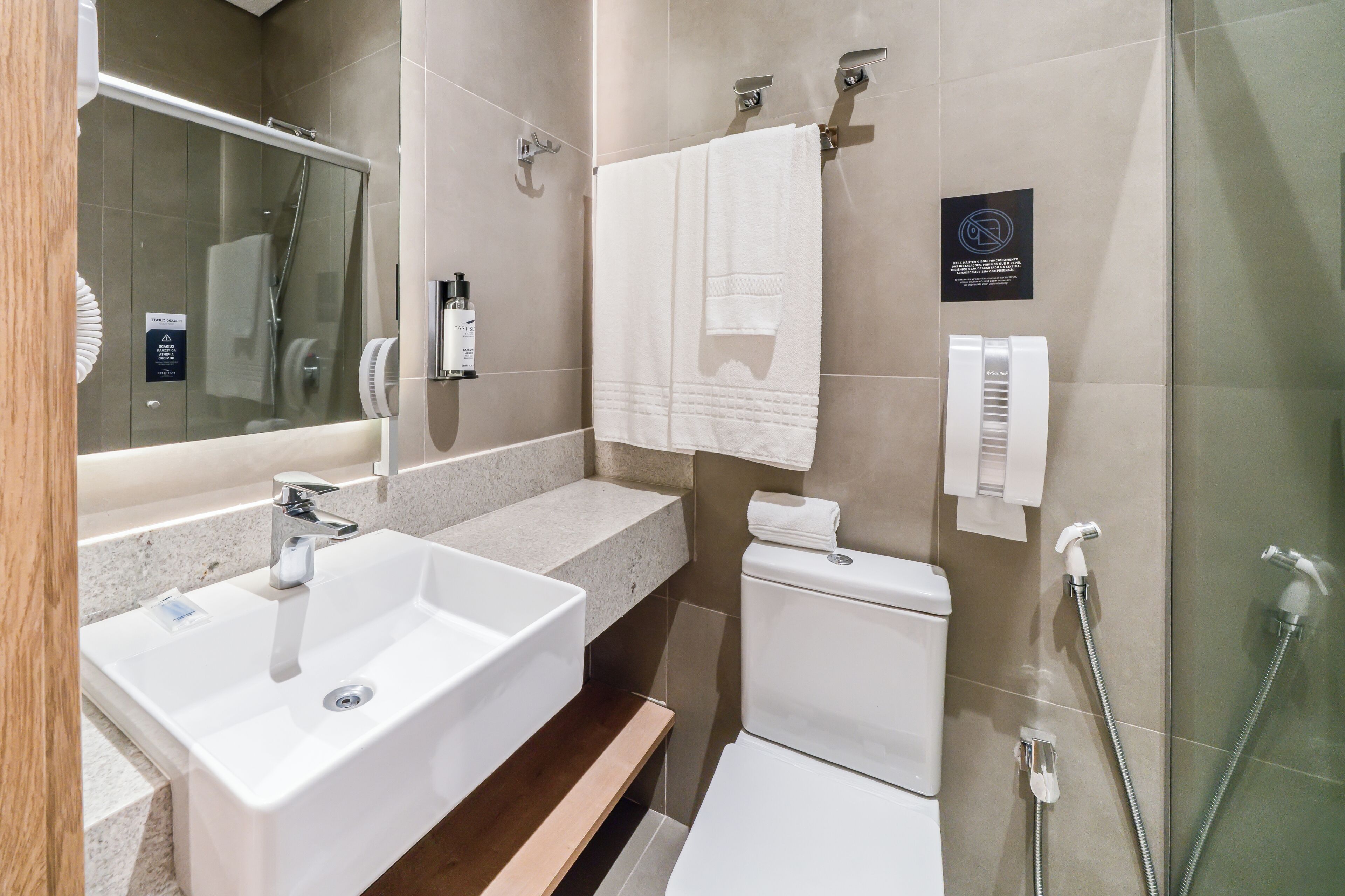 A modern bathroom with a double sink, a toilet, a glass shower enclosure, and a towel rack.