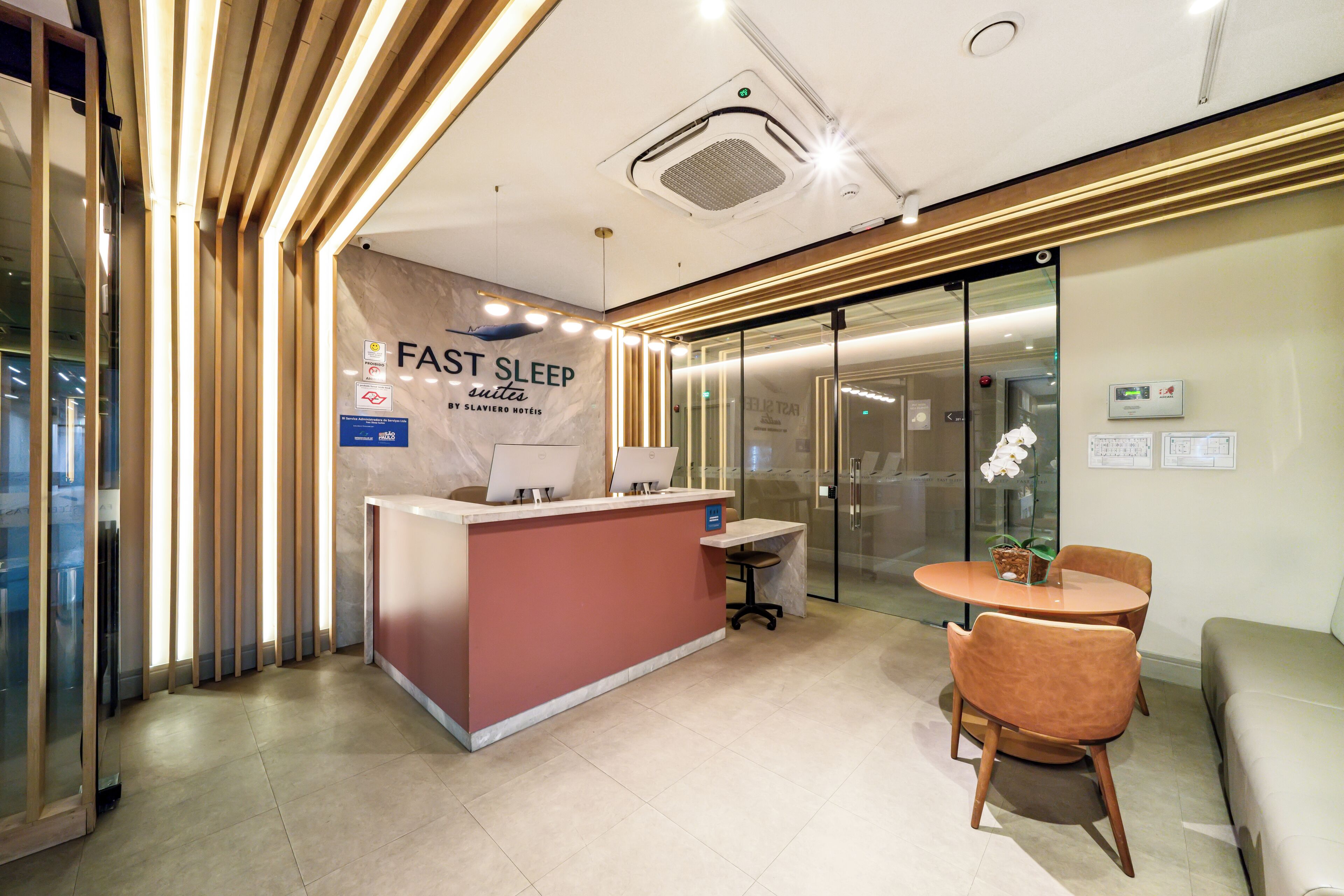 A reception desk with a sign for 'FAST SLEEP by Slaviero Hotel,' a glass door, a round table with chairs, and a sofa.