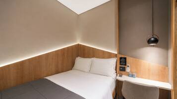 A hotel room with a bed, bedside table, chair, and a pendant light.