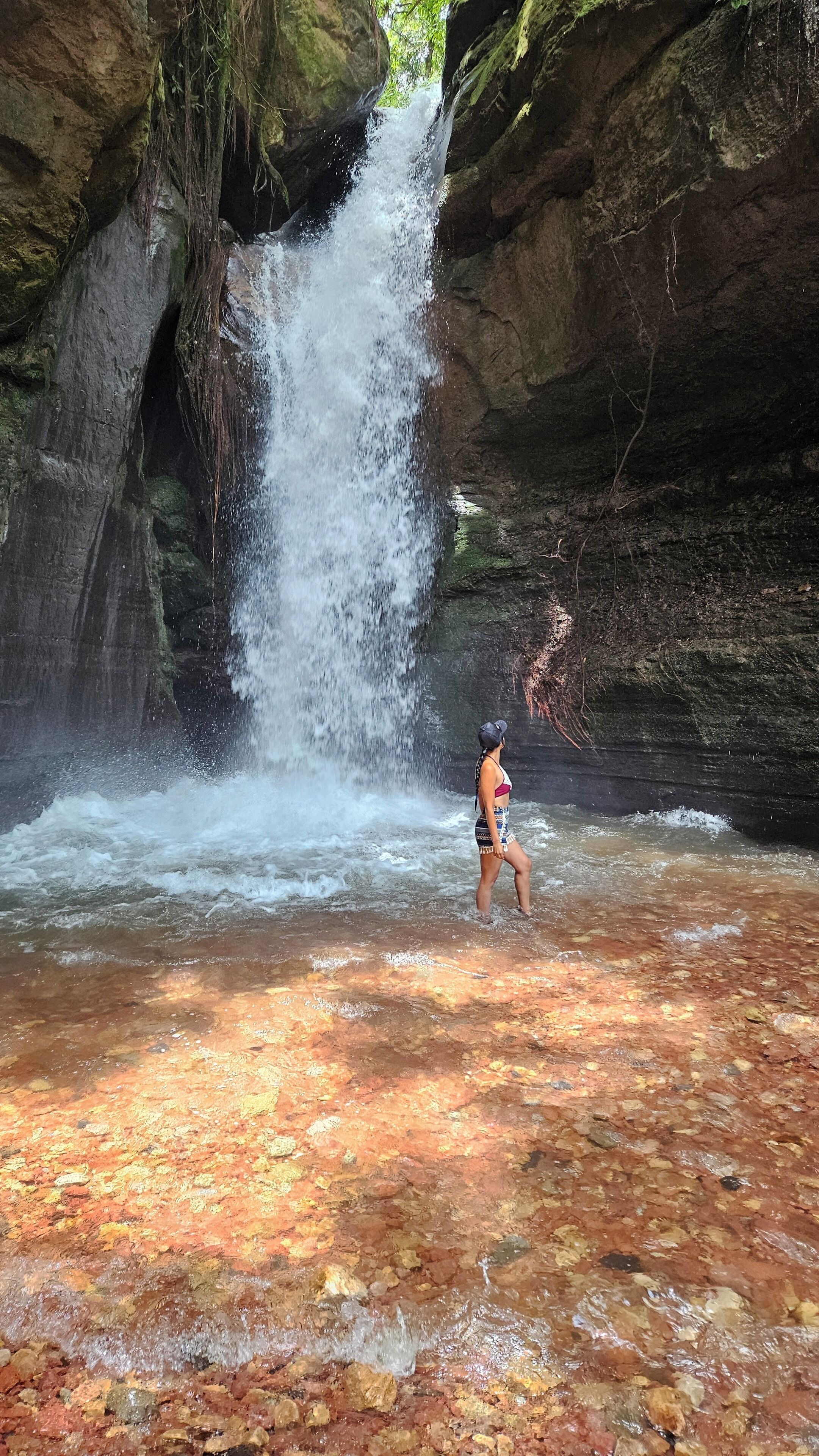 A person standing in a shallow pool of water with a waterfall in the background.