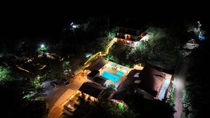 Vista aérea de un resort con piscina, mobiliario exterior y un sendero bien iluminado.
