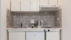 A compact kitchen with white cabinets, a built-in dishwasher, a coffee maker, and a kettle. - Castello On The Beach (Naxos)