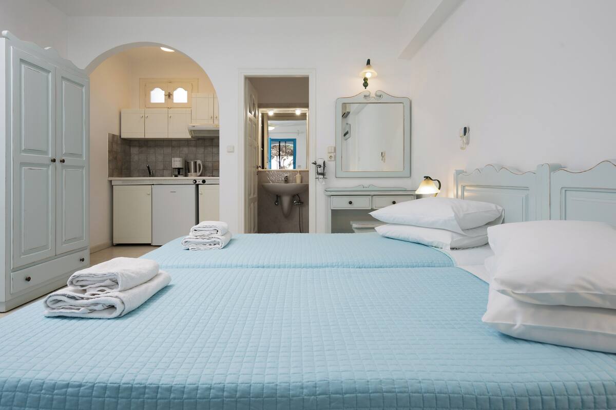 Habitación de hotel con dos camas, kitchenette, baño y espejo.