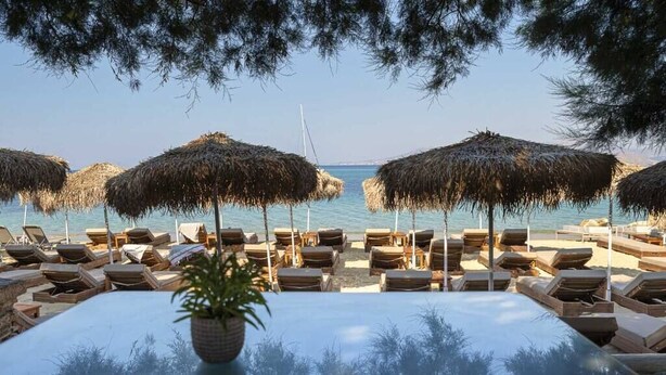 A beachside lounge area with sun loungers and thatched umbrellas, overlooking the sea. - Castello On The Beach (Naxos)