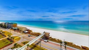 Een kustweg met uitzicht op het strand, een voetgangersbrug en gebouwen op de achtergrond.