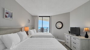 Et hotelværelse med to senge, et fjernsyn, et skrivebord og en balkon med havudsigt.