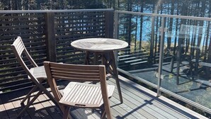 A wooden deck with a glass balustrade overlooking a forested area.