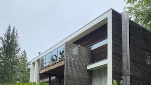 A modern building with a balcony, surrounded by lush greenery and stone steps.