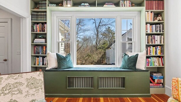 Una habitación con un asiento empotrado junto a la ventana, estanterías y un sillón estampado.