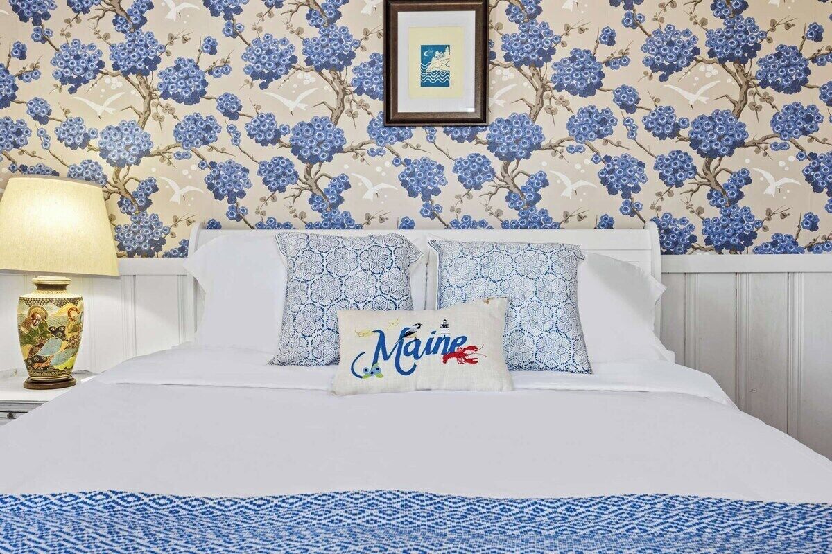 Een bed met twee kussens, waarvan één met de tekst 'Maine', een ingelijst plaatje erboven en een lamp aan de linkerkant.