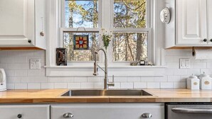 Una cocina con armarios blancos, un lavamanos de acero inoxidable y una encimera de madera.