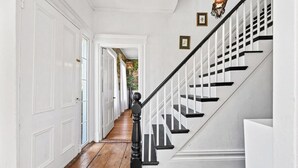 Un pasillo con piso de madera, puertas blancas, una escalera con barandas negras y una lámpara fijada a la pared.