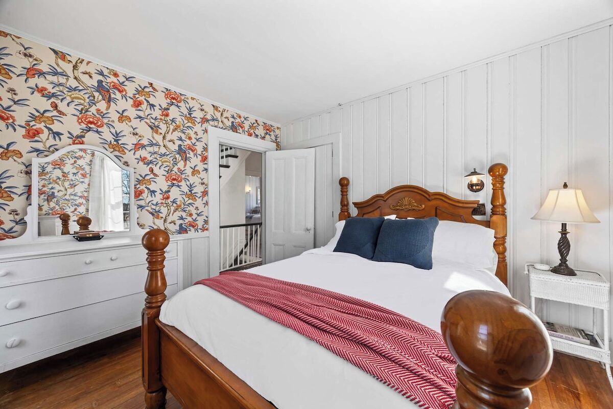 A bedroom with a wooden bed, a mirror, a dresser, and a floral wallpaper.