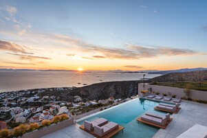 Un resort con piscina infinita, sillas de descanso y vistas al mar al atardecer.