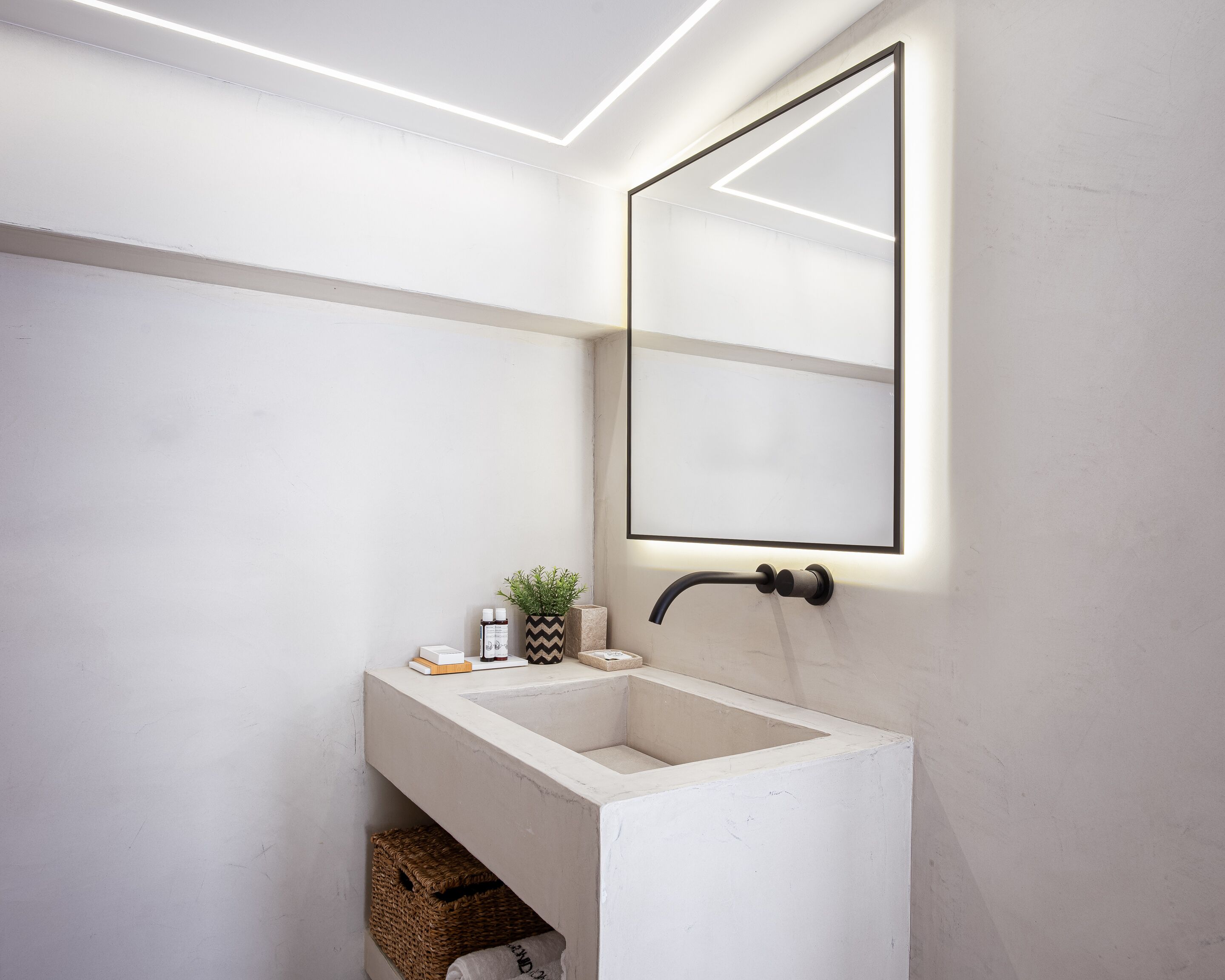 A modern bathroom with a white sink, a mirror, and a potted plant.