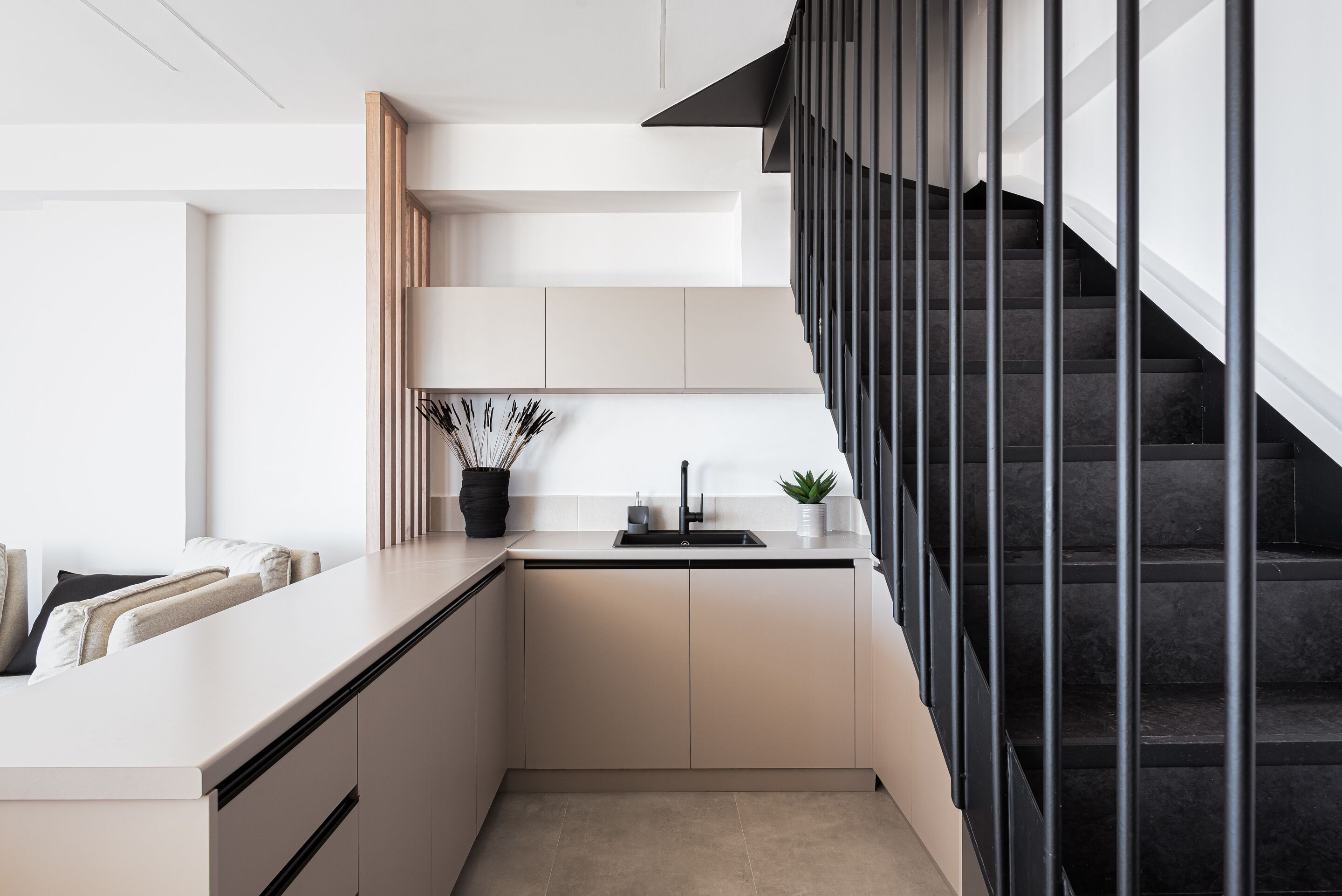 Una cocina moderna con isla integrada, escalera negra y diseño minimalista.