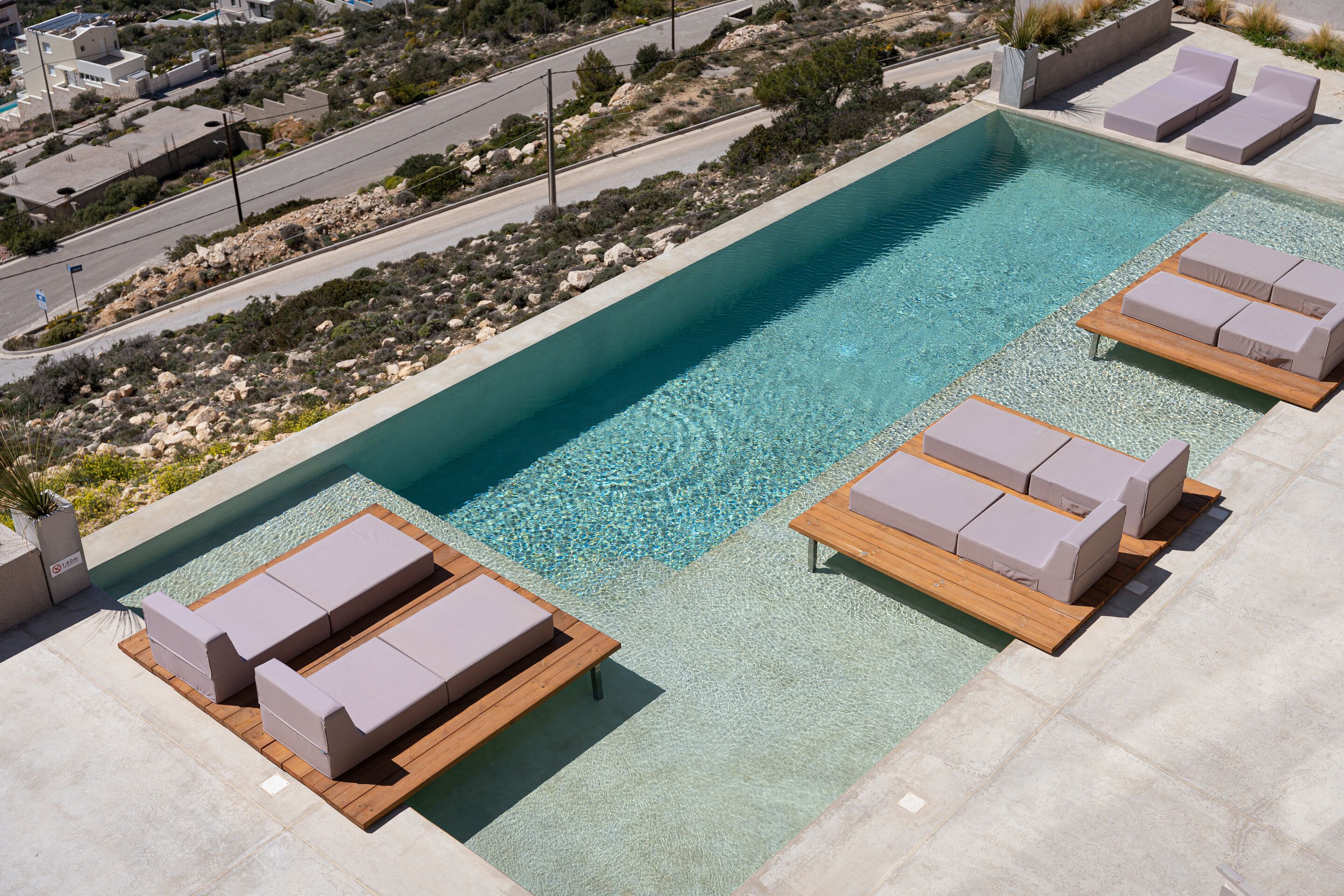 Une piscine sur le toit, avec une eau cristalline, entourée de chaises longues et bordée d’une plage de galets.