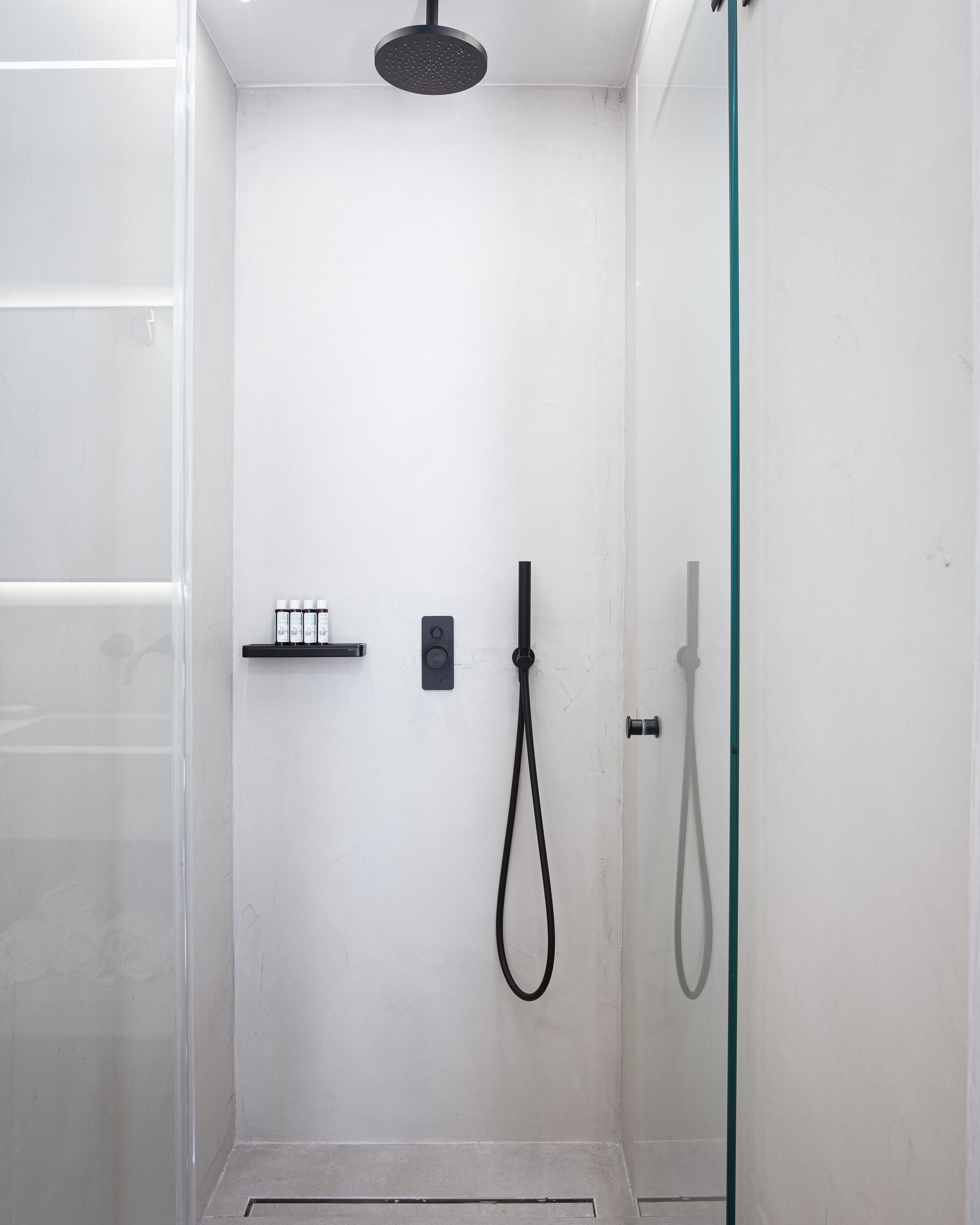 A modern shower with a handheld showerhead and a fixed showerhead, a control panel, and a glass door.