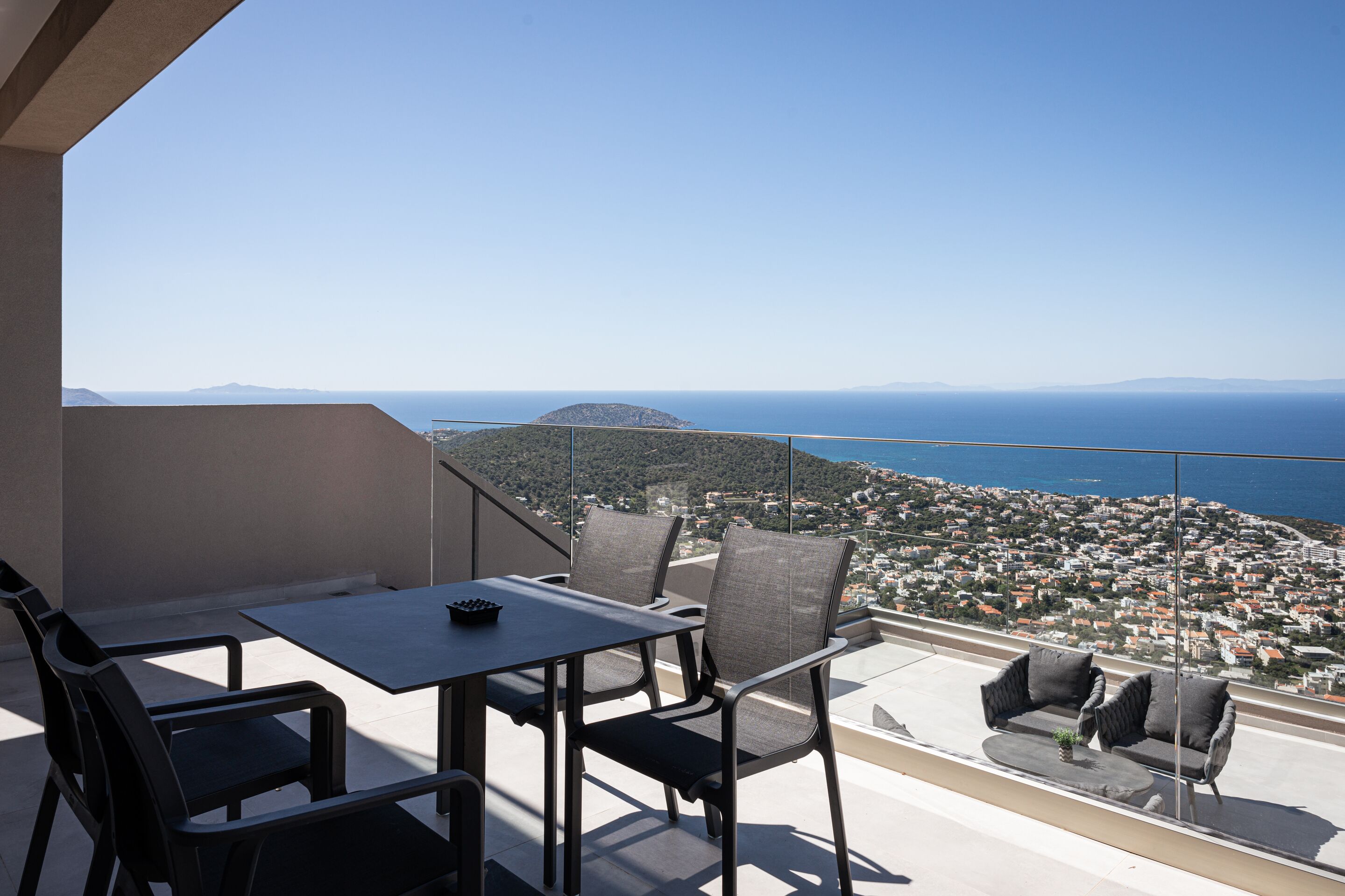 A balcony with a table and chairs, offering a view of a coastal town and the sea.