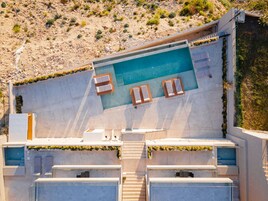 Una piscina en la azotea con sillones de descanso y vistas a una ladera rocosa.
