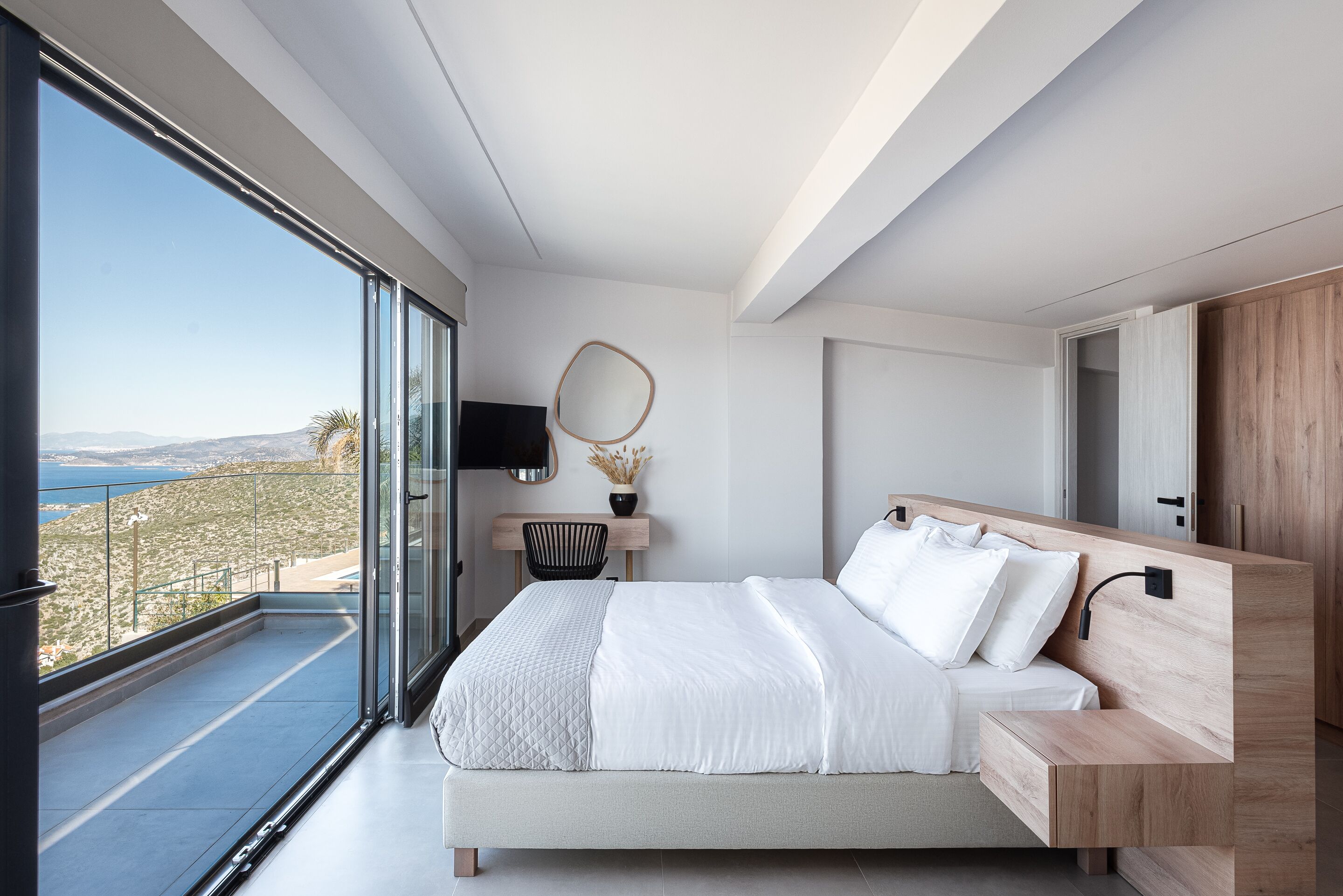 A modern bedroom with a large bed, a desk, and a view of the outdoors.