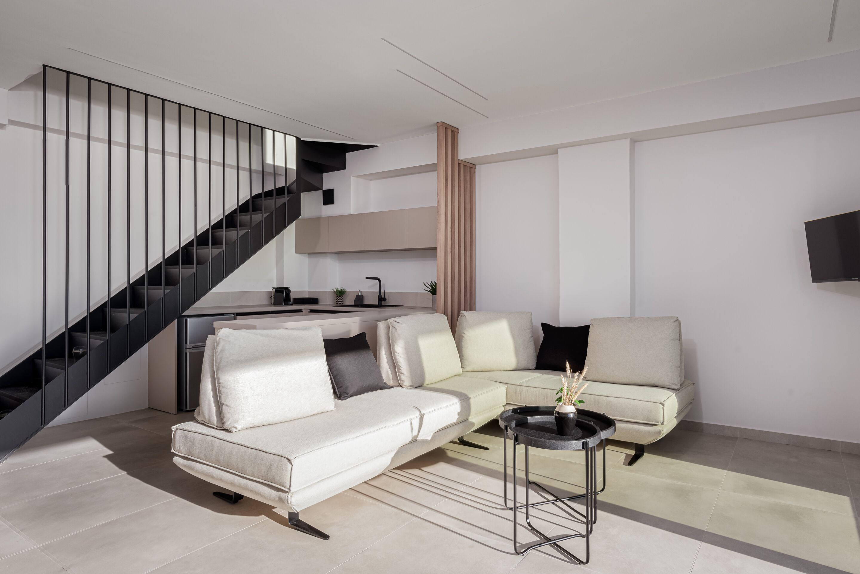 Een moderne woonkamer met een witte bank, een zwarte trap en een keuken op de achtergrond.