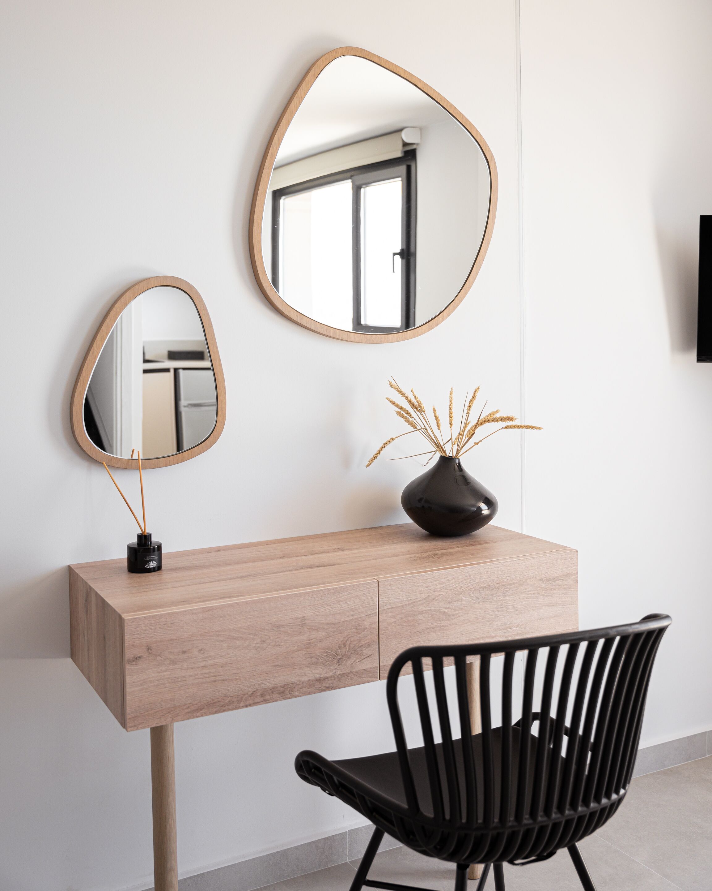 Un escritorio moderno con detalles de madera, una silla negra y dos espejos fijos a la pared.