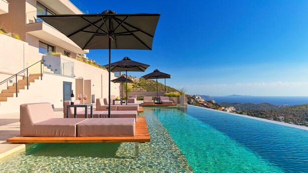 Una piscina infinita lujosa con agua cristalina, asientos al aire libre y sombrillas, con vistas a una ladera pintoresca.
