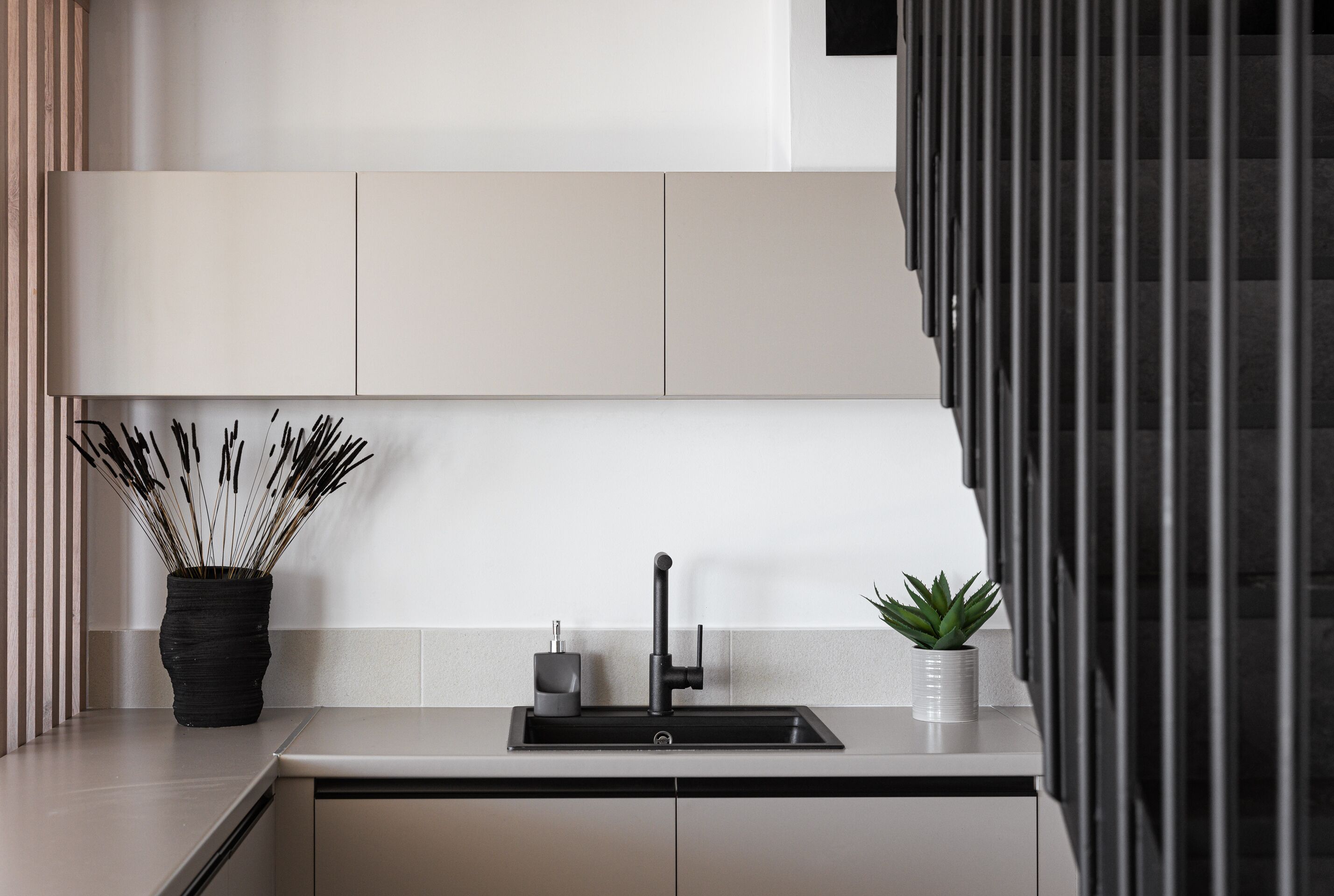 A modern kitchen with a black faucet, a potted plant, and a vase with reeds.